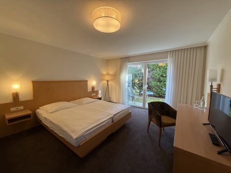Helles Zimmer mit Doppelbett, Schreibtisch und Zugang zu einem Garten.