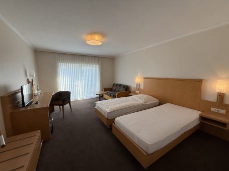 Helles Zimmer mit zwei Einzelbetten, Tisch, Stühlen und einem Fernseher.