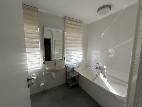 Helles Badezimmer mit Waschbecken, Spiegel und Fensterjalousien.