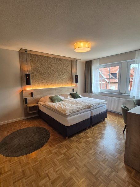 Helles Hotelzimmer mit Doppelbett, zwei Kissen und modernen Möbeln.